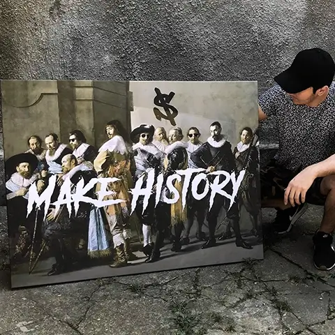 Un artist stând lângă un tablou care reinterpretează o lucrare clasică, cu textul „MAKE HISTORY” scris în stil graffiti. Tabloul include mai multe personaje din picturi celebre, iar artistul poartă o pălărie neagră și îmbrăcăminte lejeră. Fundalul este un perete gri.